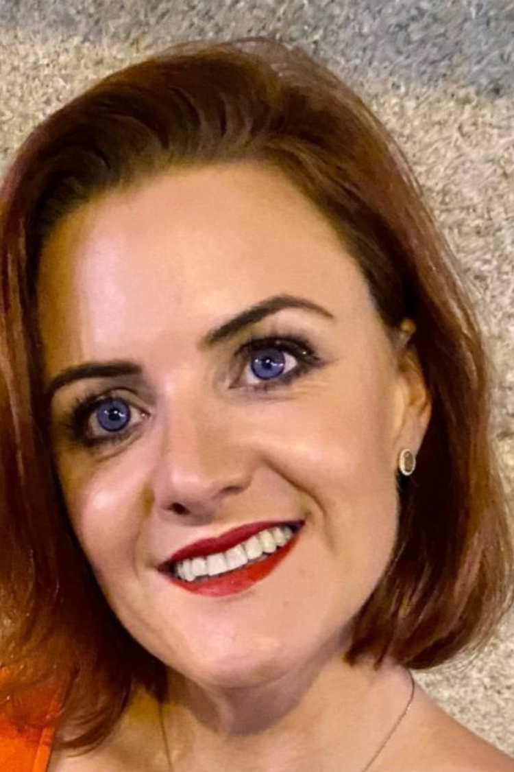 A headshot of Christine, smiling at the camera. She has short auburn hair and blue eyes.