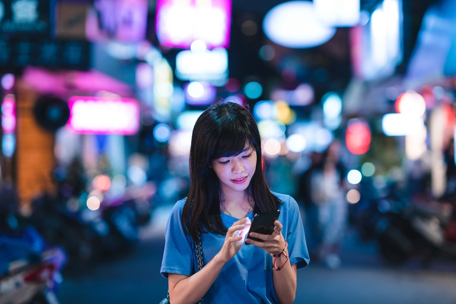 A young woman using her phone in the city at night