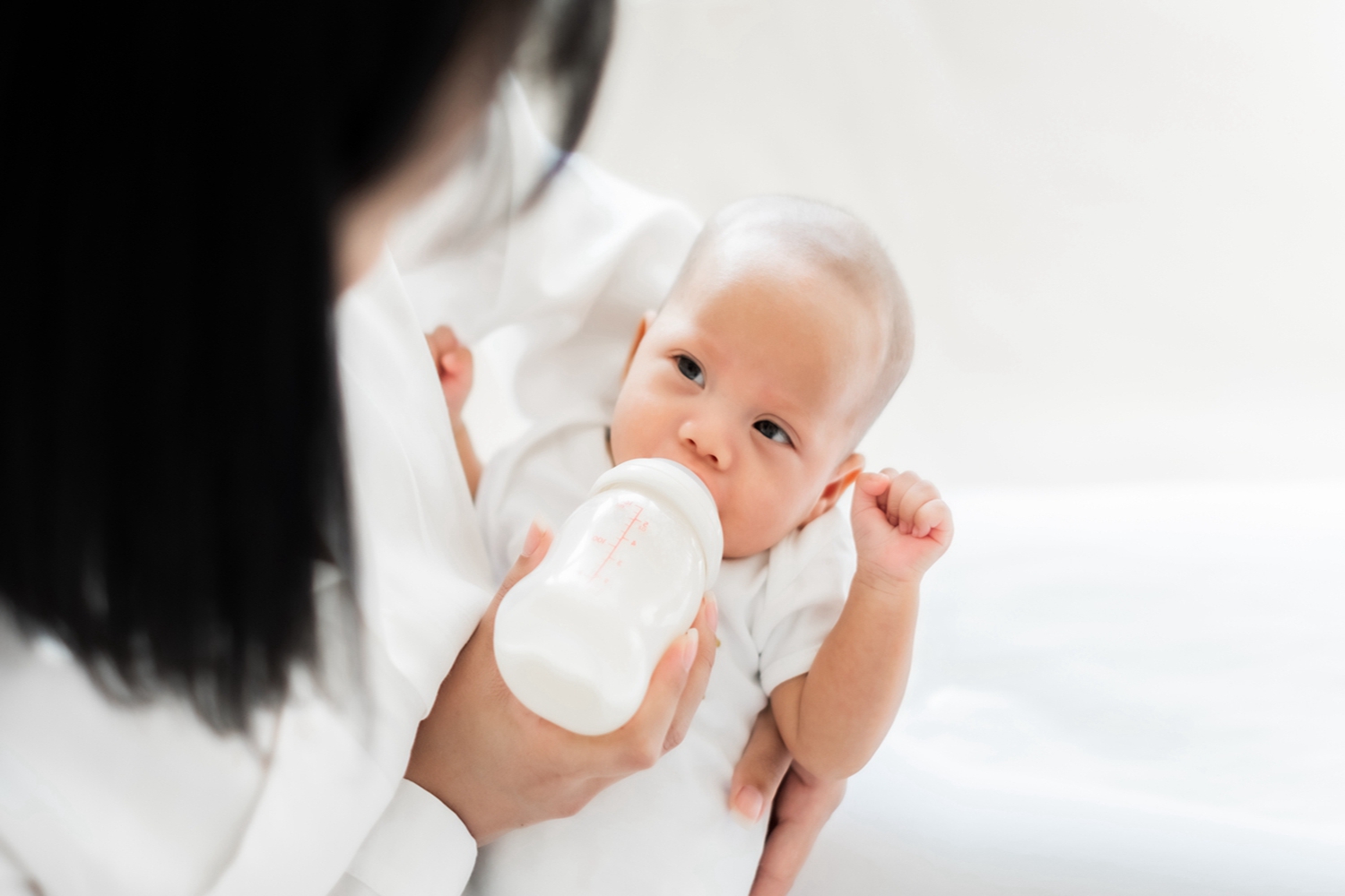 Mother feeding asian baby with bottle of milk, banner copy space