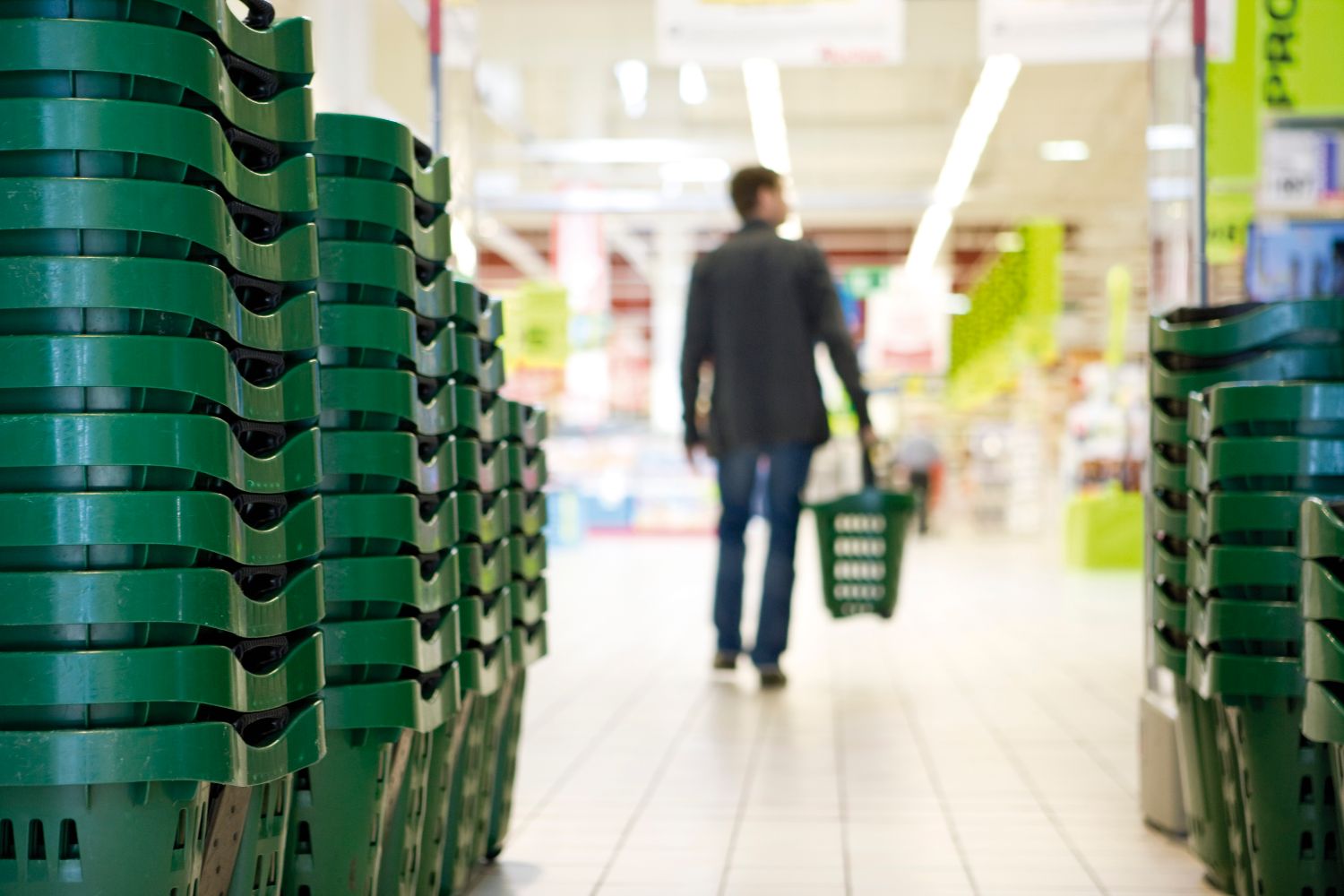 Man walking into a supermarket holding a green shopping basket