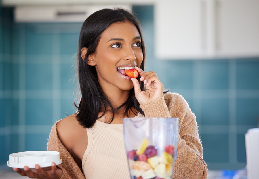 Woman eating a strawberry while making a smoothie