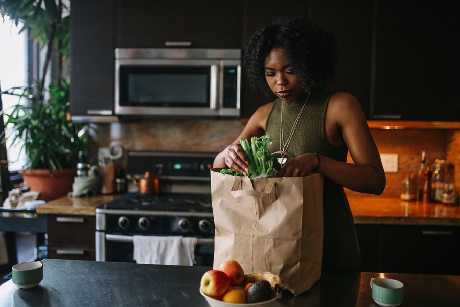 Woman unpacking fruit from a brown paper shopping bag in kitchen