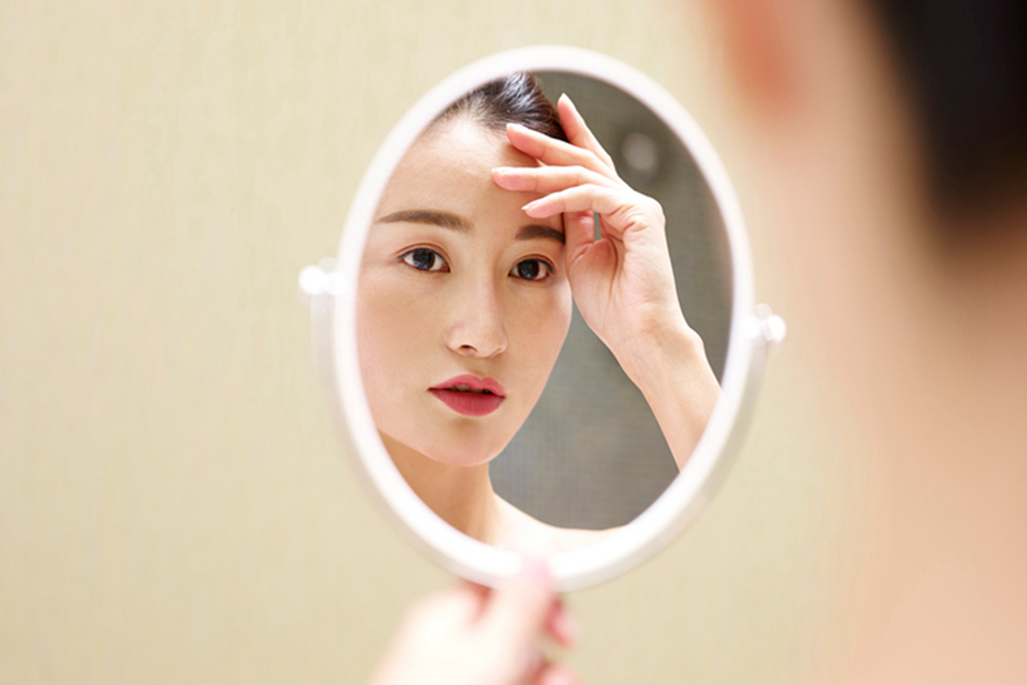 East Asian woman looking into hand-held mirror