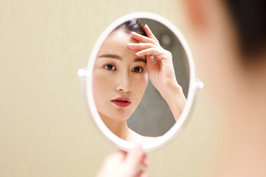 East Asian woman looking into hand-held mirror